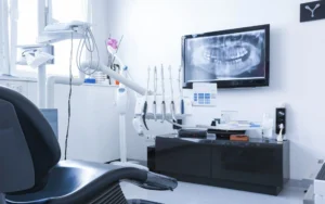 Modern dental clinic setup with a patient chair, dental equipment, and a large screen displaying a dental X-ray on the wall.