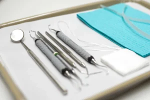 Set of dental tools, including a dental mirror, scalers, gauze, and a blue dental bib, neatly arranged on a tray in preparation for a dental procedure.