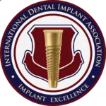 Logo of the International Dental Implant Association featuring a gold dental implant in the center, surrounded by a maroon and blue circular border with the text 'International Dental Implant Association' and 'Implant Excellence'.
