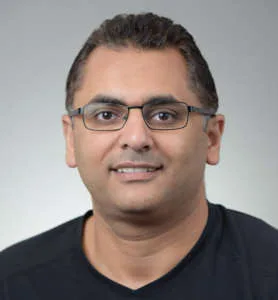 Portrait of Dr. Tarek Fahmy, a dentist, wearing glasses and a black shirt, smiling in front of a neutral background.